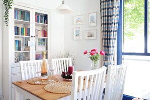 A dining area with a wooden table, white chairs, a bottle of wine, and a vase of flowers.