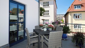Ein Balkon mit Korbmöbeln, einem Tisch mit Blumen und Blick auf benachbarte Gebäude.