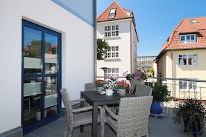 A balcony with wicker furniture, a table with flowers, and a view of neighboring buildings.