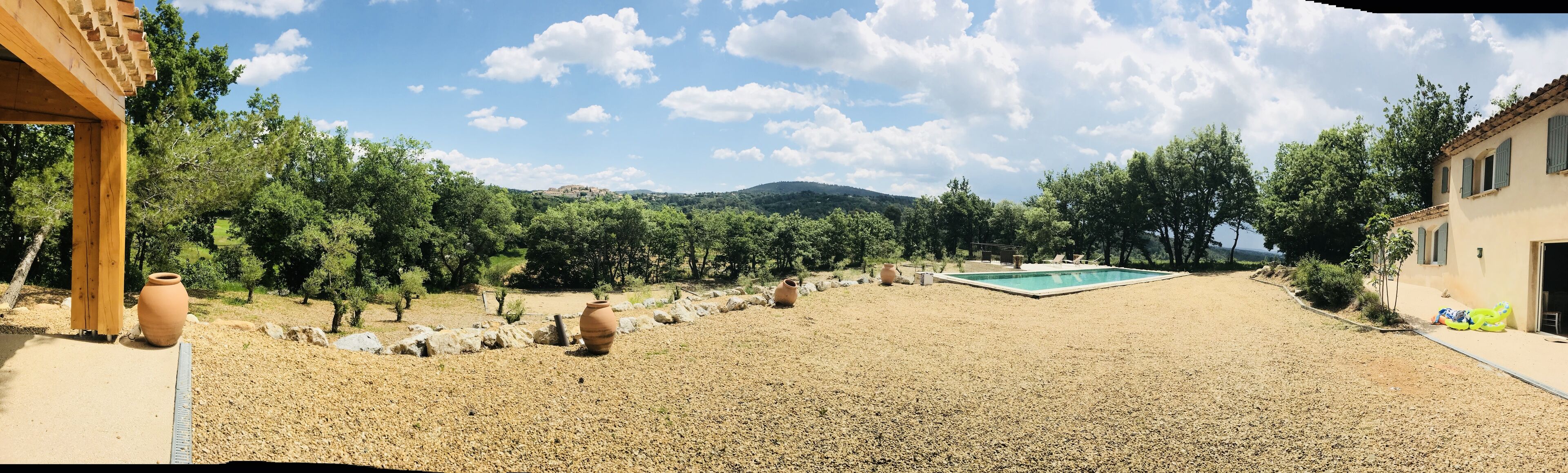 A courtyard with a swimming pool, surrounded by trees and a view of distant hills.