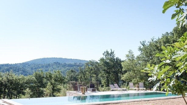 Una piscina con vista su una collina boscosa, circondata da alberi e un pergolato.