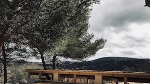 Un parco con una panchina in cemento, un piccolo giardino e una vista su un paesaggio collinare sullo sfondo.
