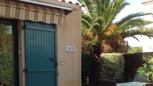 Un bâtiment avec une porte numérotée, un patio comprenant une table et des chaises, et un palmier en arrière-plan.