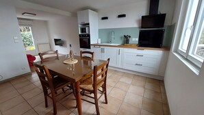 Une cuisine moderne avec des meubles blancs, une table à manger en bois et une grande fenêtre.