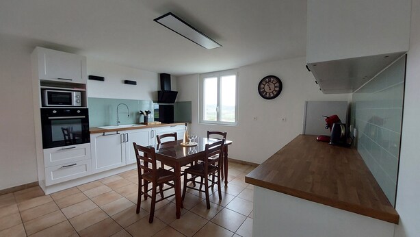 Une cuisine avec des meubles blancs, une table à manger avec des chaises, un four à micro-ondes, un four traditionnel et une horloge au mur.