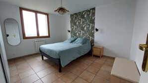 Une chambre à coucher comprenant un lit, une fenêtre, un radiateur, une petite table de chevet et un luminaire fixé au mur.