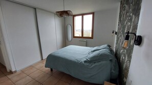Un dormitorio con cama, ventana, radiador y lámpara fijada a la pared.
