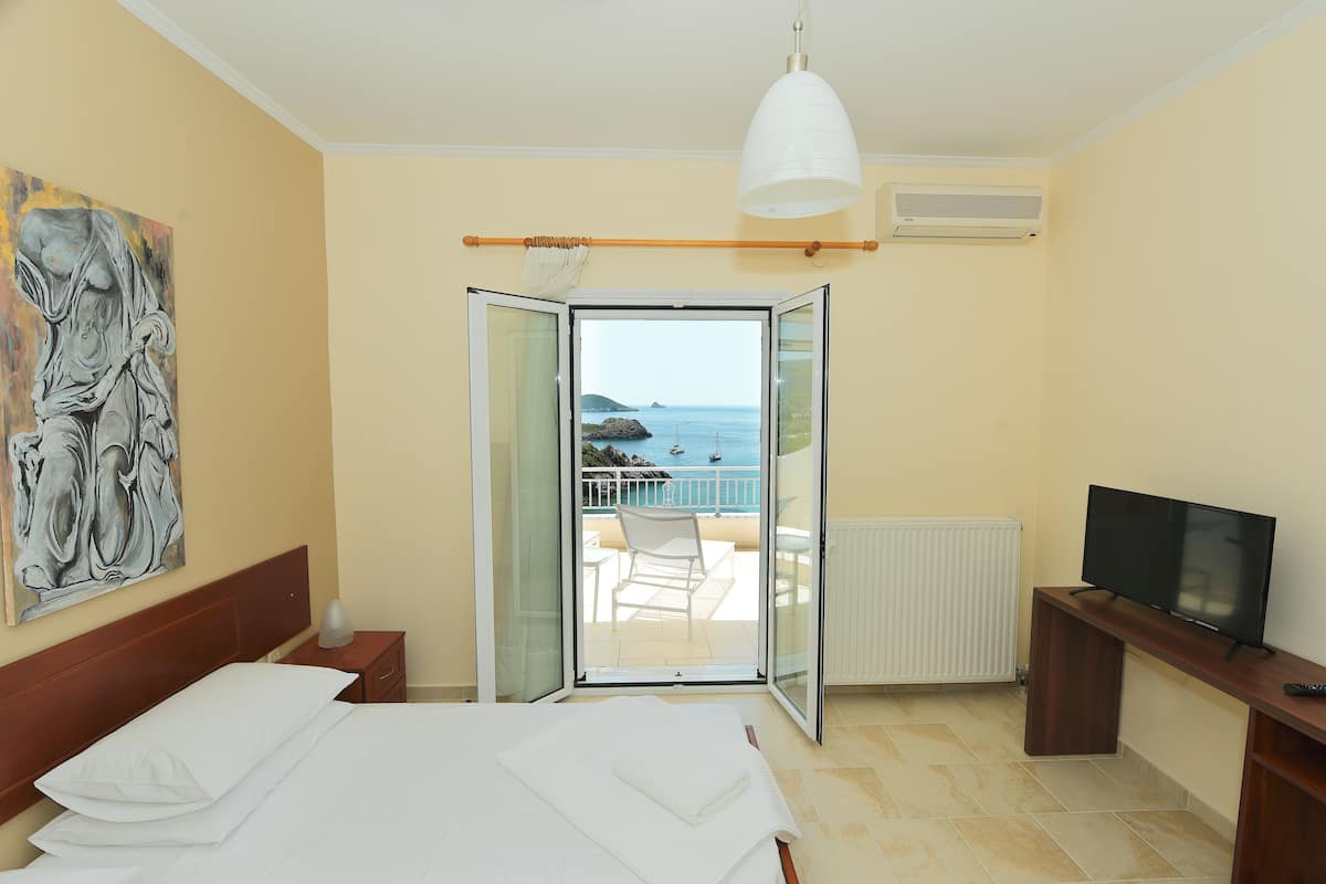 A hotel room with a bed, a TV, a painting, and a balcony with a view of the sea.