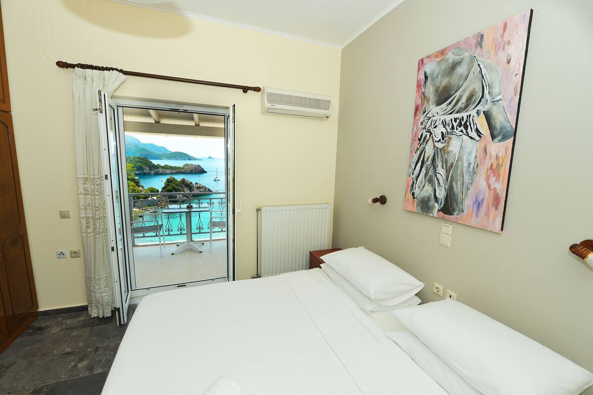 A hotel room with a bed, a painting, a view of a pool and mountains, and a window with curtains.
