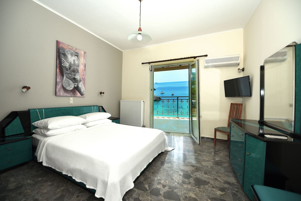 A bedroom with a bed, a TV, a desk, and a view of the sea.