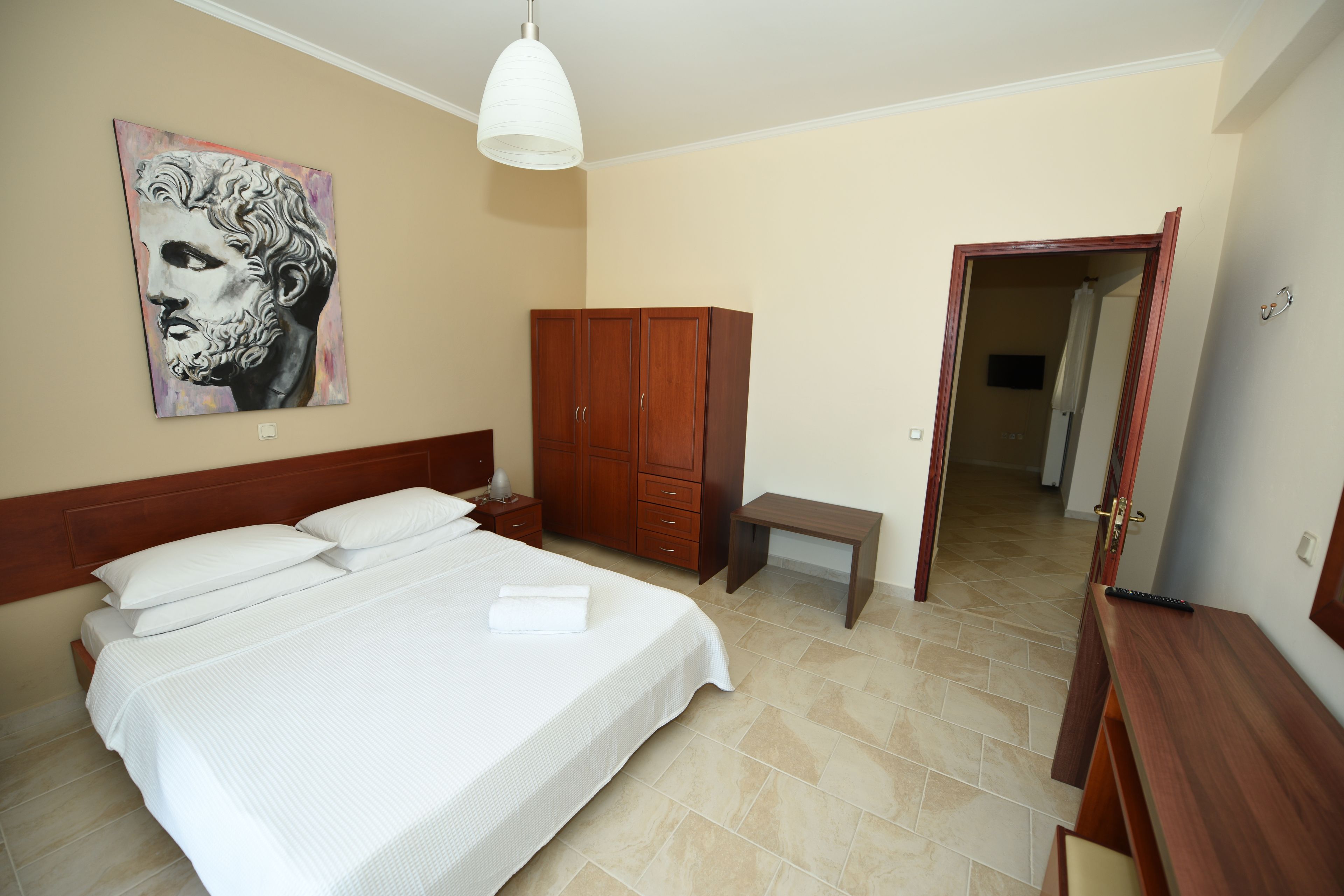 A bedroom with a large bed, wooden wardrobe, bedside table, and a painting on the wall.