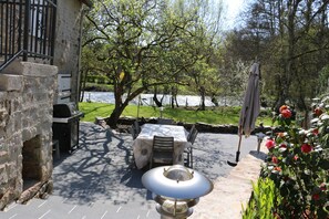 Eine Terrasse im Freien mit einem Steingrill, einem Tisch mit Stühlen und einer dekorativen Lampe.