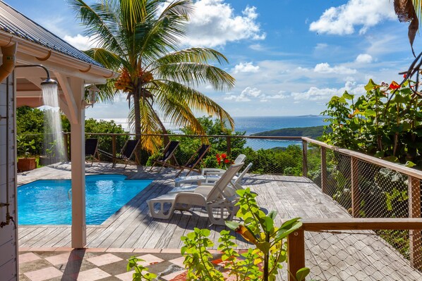 Une terrasse en bois avec une piscine, des chaises longues et une vue sur l’océan.