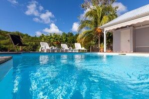 Une piscine à l’eau d’un bleu cristallin, entourée de chaises longues blanches et d’un palmier.