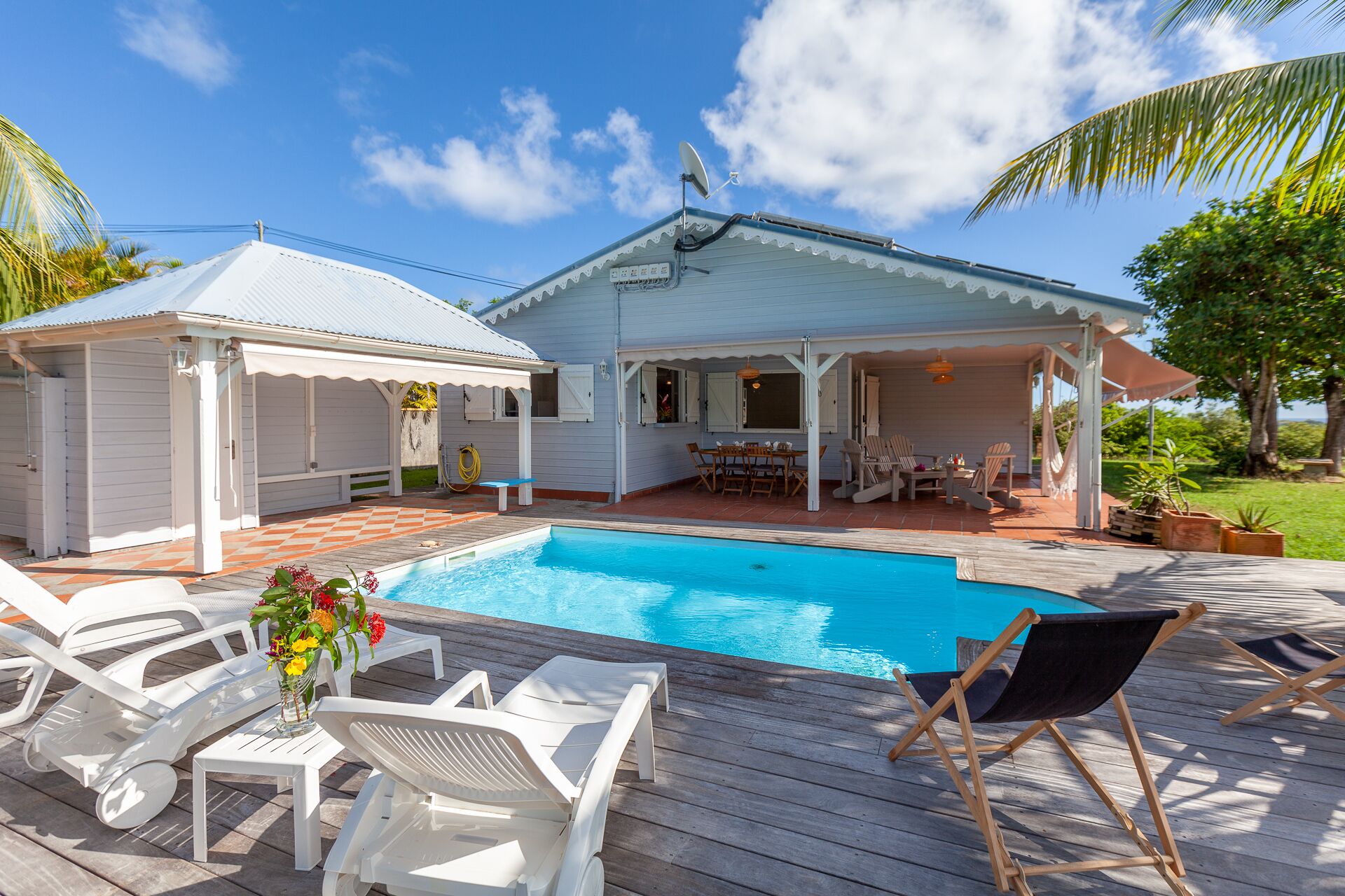 Un espace aménagé au bord de la piscine, comprenant une piscine, des chaises longues, une terrasse couverte et un petit abri de jardin.