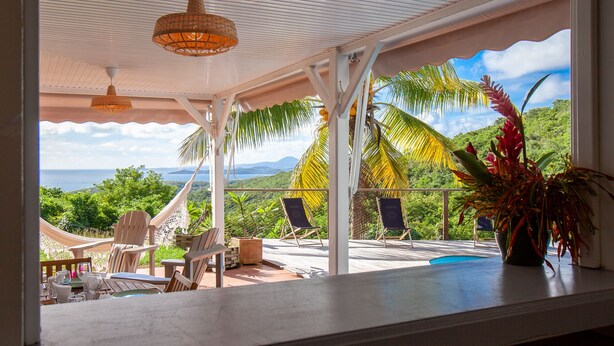 A covered outdoor seating area with chairs and tables, overlooking a lush landscape and the sea. - Villa Vue Sauvage in Tartane, in the Caravelle nature reserve. (LA TRINITÉ)