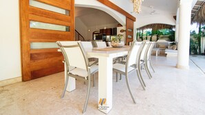 Un coin repas avec une table et des chaises blanches, une porte en bois dotée de panneaux de verre et un ventilateur de plafond.