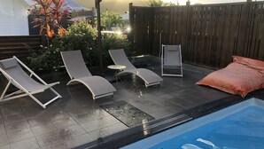 Un jardin avec une piscine, deux chaises longues, une petite table et un grand parasol.