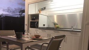 Une cuisine moderne avec un coin repas, dotée d’une grande fenêtre, d’appareils électroménagers en acier inoxydable et d’un panier de fruits posé sur le plan de travail.