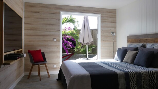 Une chambre à coucher comprenant un lit, une chaise, un bureau et une fenêtre donnant sur des fleurs et un palmier.