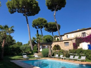 A pool area with lounge chairs, a stone building, and tall trees.