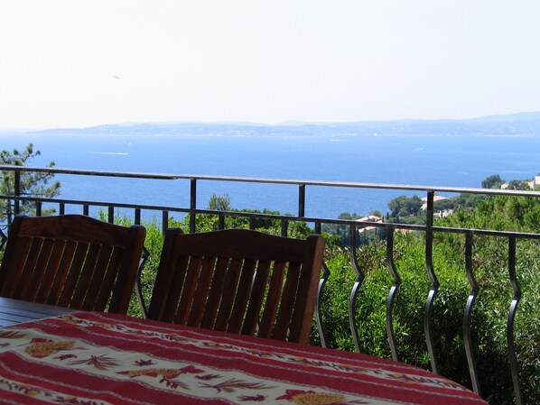 Un balcon avec une table et des chaises, donnant sur un paysage côtier avec des collines à l’horizon.