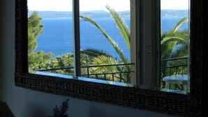 Une fenêtre donnant sur un paysage côtier, avec des palmiers et une étendue d’eau.