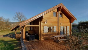 A wooden cabin with a sloped roof, a deck, and a patio area.