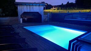 A swimming pool with a wooden deck and a covered area with a bench.