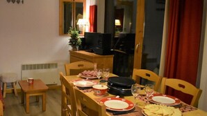 Un comedor con una mesa dispuesta para dos personas, un taburete pequeño, un radiador y un televisor al fondo.