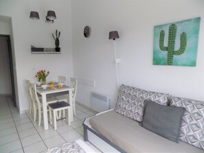 Una stanza con un letto, un tavolo da pranzo con sedie, un quadro di un cactus e una sveglia a parete.
