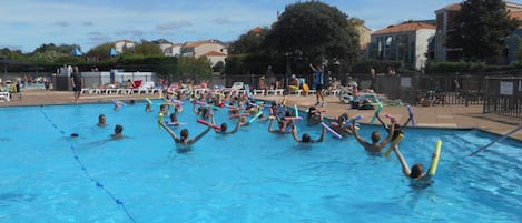 A swimming pool with people engaged in water activities, surrounded by a fence and buildings.