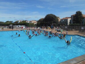 Una piscina con persone che praticano attività acquatiche, circondata da una recinzione e degli edifici.