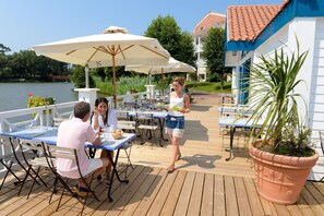 A deck with tables and chairs, a large umbrella, and a potted plant.