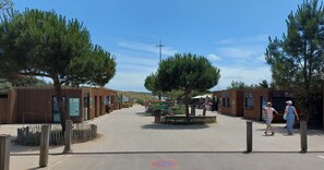 A pathway leading to a building with a wooden facade, a signboard, and a small seating area with tables and chairs.