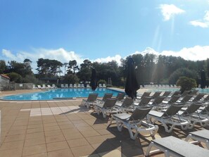 A swimming pool with sun loungers and a covered area, surrounded by trees.