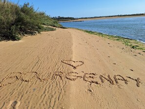 Une plage de sable avec des empreintes et le mot « DOURGENAY » écrit dans le sable.