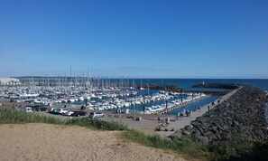Ein Yachthafen mit zahlreichen Booten, einem steinernen Wellenbrecher und einem strahlend blauen Himmel.
