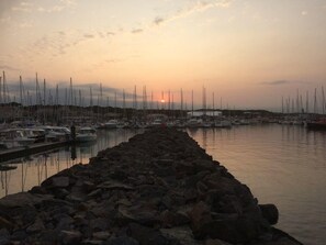 Un port de plaisance où des bateaux sont amarrés le long d’une digue rocheuse, au coucher du soleil.