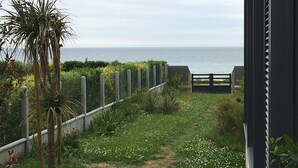 En sti der fører til en strand med et træhegn og en port, omgivet af grønt og et palmetræ.