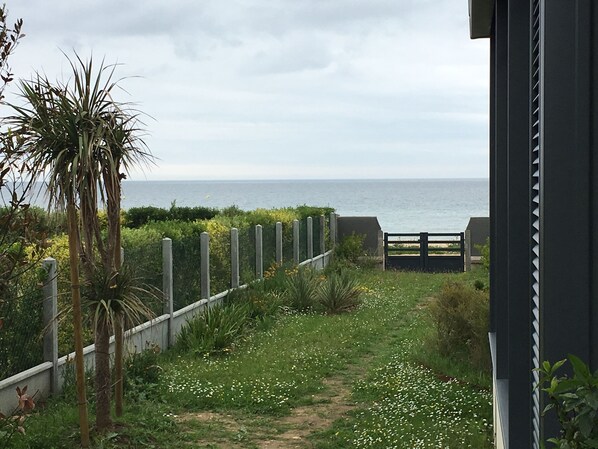 A pathway leading to a beach with a wooden fence and a gate, surrounded by greenery and a palm tree. - Normandy Waterfront, fantastic view, direct access to the beach Appt 3 bedrooms for 6 (Hermanville-sur-Mer)