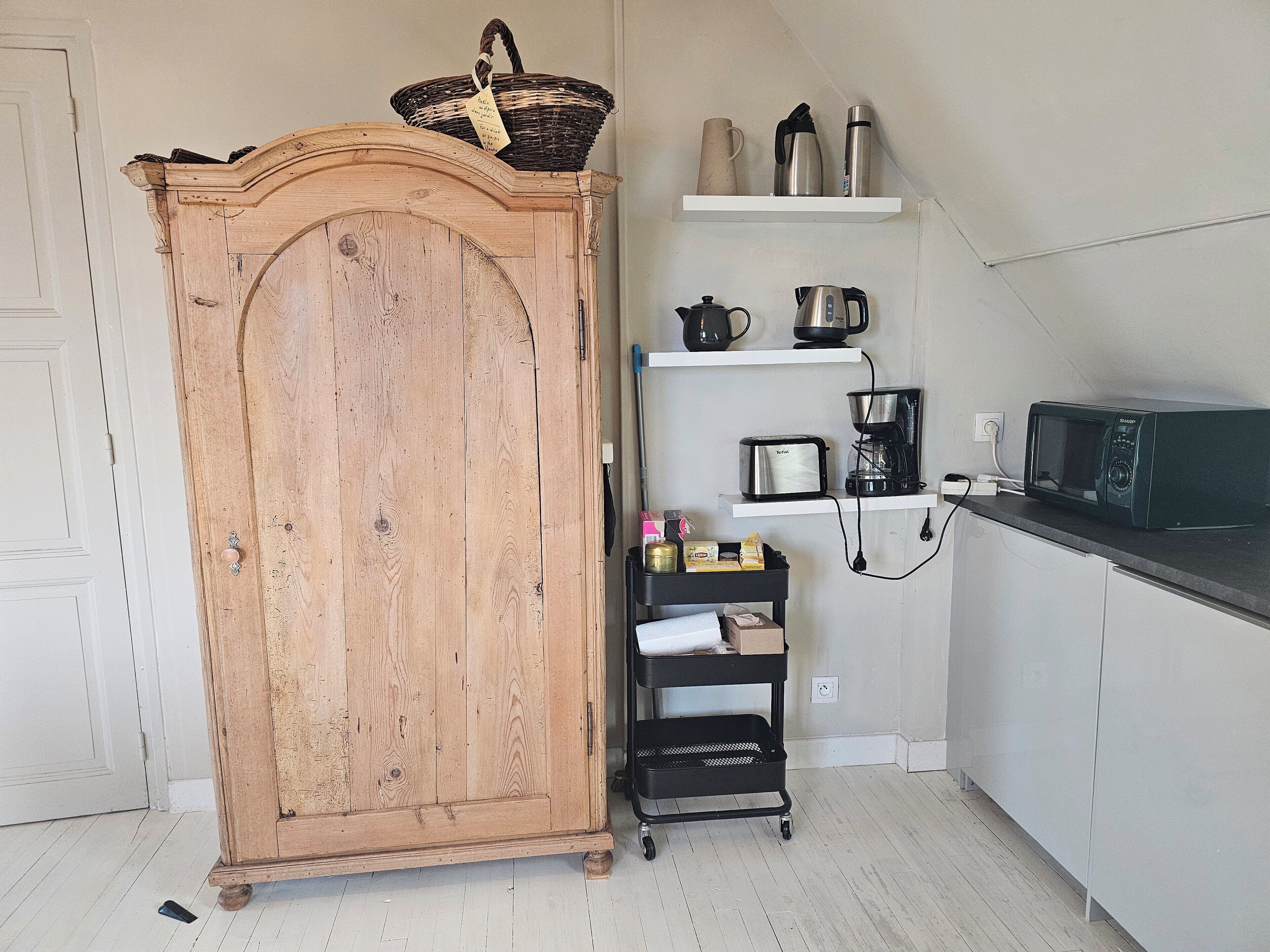 Une cuisine avec des meubles de rangement en bois, un chariot noir et divers appareils électroménagers, comme un grille-pain, une machine à café et un four à micro-ondes.