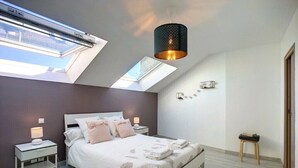 A modern bedroom with a skylight, a bed with white bedding, a bedside table with a lamp, and a small stool. - Beautiful duplex near the sea (the islands) (Donville-les-Bains)