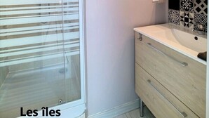 A modern bathroom with a glass shower enclosure, a white sink with a black and white patterned backsplash, and a wooden vanity with drawers. - Beautiful duplex near the sea (the islands) (Donville-les-Bains)