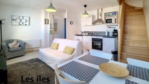 A compact living space with a kitchenette, a dining area, and a seating area with a sofa and a chair. - Beautiful duplex near the sea (the islands) (Donville-les-Bains)