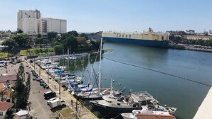 A marina with boats docked, a large ship named 'EUKOR' in the background, and a building with a clock tower. - Luxury Apartment at Riviera Colonial (Santo Domingo Este)
