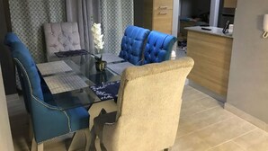 A dining area with a glass table, blue upholstered chairs, and a beige chair. - Luxury Apartment at Riviera Colonial (Santo Domingo Este)