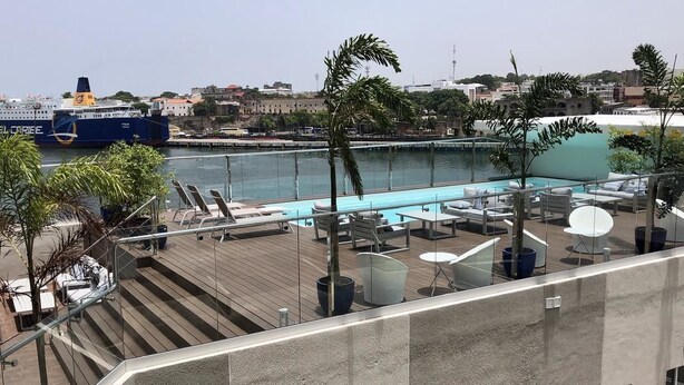 A rooftop pool area with lounge chairs and a view of a large ship named 'FERRIES DEL CORIBE' in the background. - Luxury Apartment at Riviera Colonial (Santo Domingo Este)