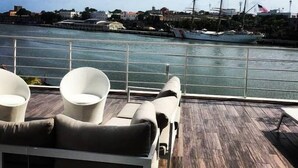 A deck with lounge chairs and a view of a harbor with ships. - Luxury Apartment at Riviera Colonial (Santo Domingo Este)