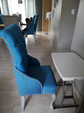 A dining area with blue upholstered chairs, a white table, and a tiled floor. - Luxury Apartment at Riviera Colonial (Santo Domingo Este)